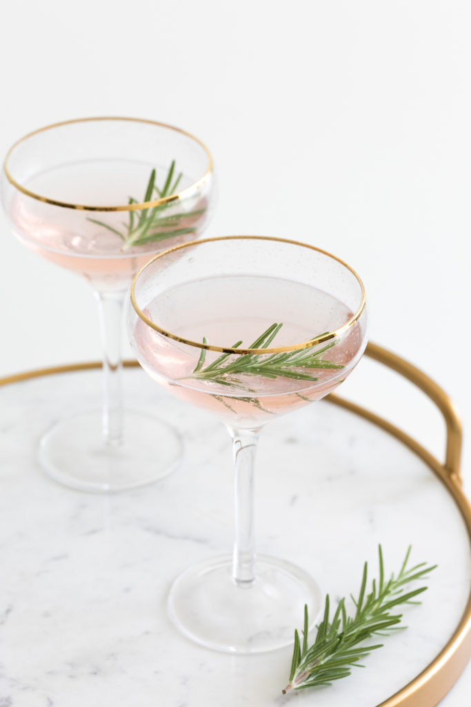A close up image of a champagne glass with champagne in it and some rosemary.