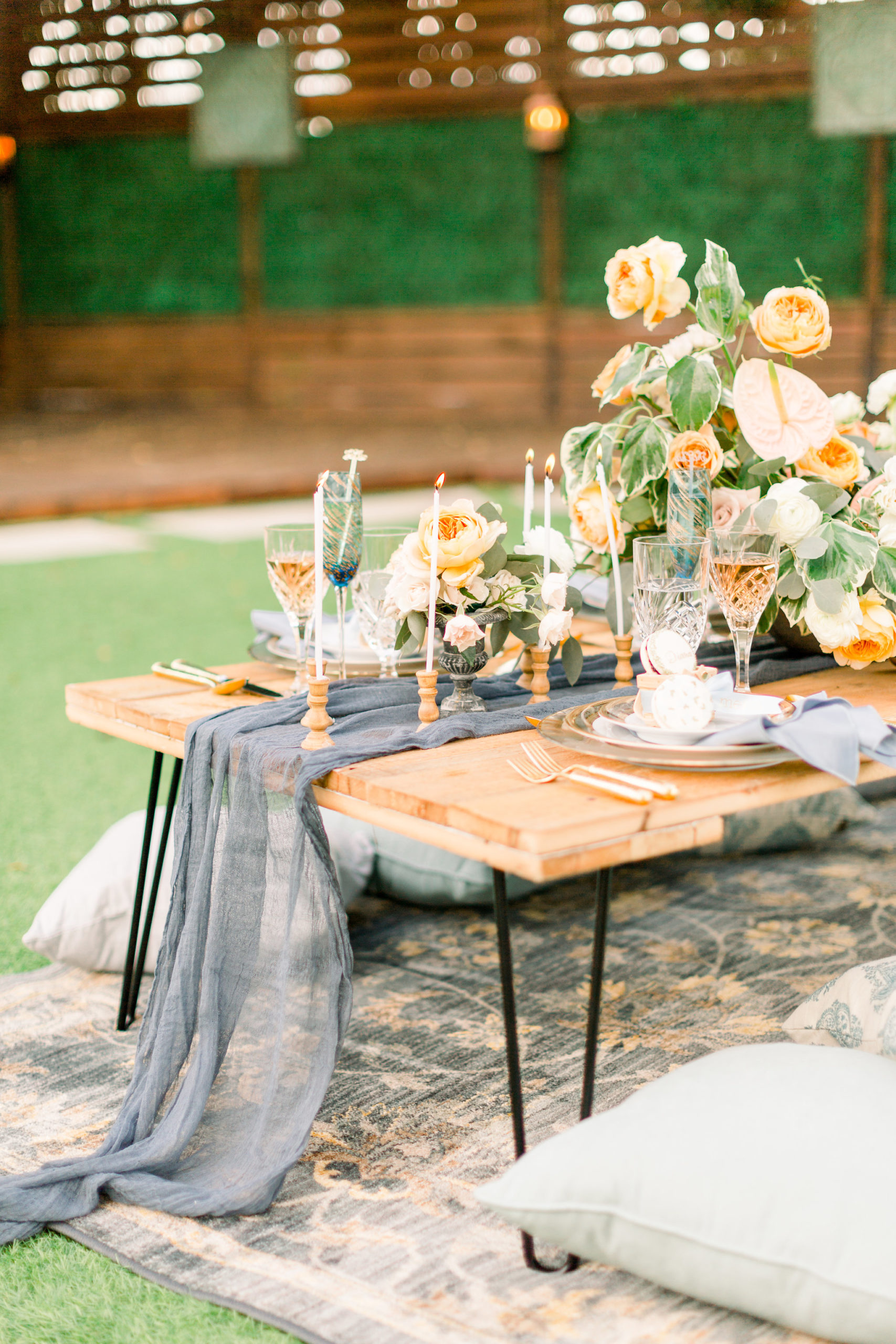 A picnic table set up on a picnic rug with floral centerpieces and wine glasses